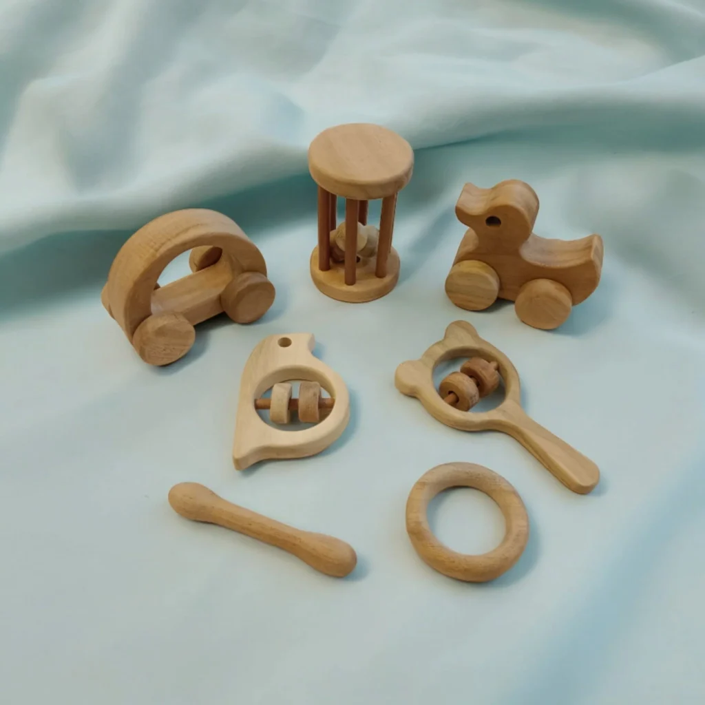 A collection of natural wooden baby toys, including a rolling car, a duck, and sensory rattles, arranged on a soft blue fabric.